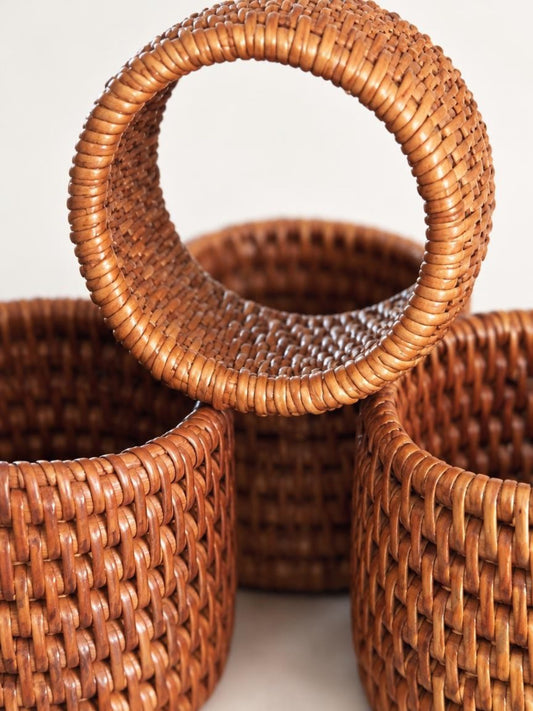 Close-up of rattan napkin rings showing the tight basketweave, wrapped rims, and natural variations in warm brown tones.