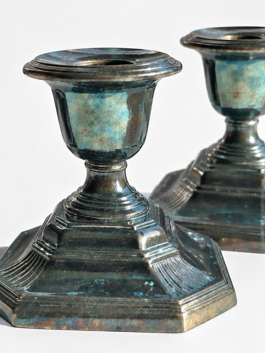 Close-up of a silverplate candlestick showing fluted corners, a stepped octagonal base, and blue-green tarnish.