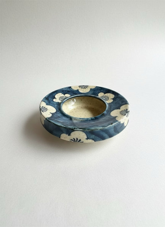 Ceramic plant water retention dish with blue and white design on a light gray background