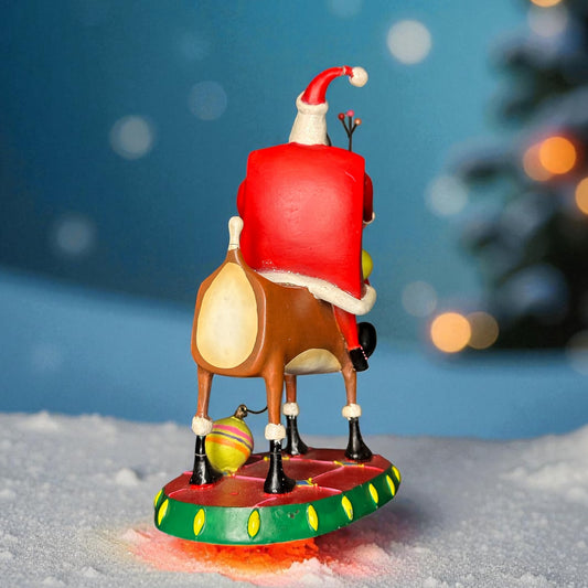 Santa Claus figurine riding a reindeer on a snowy base with a blurred Christmas tree in the background.