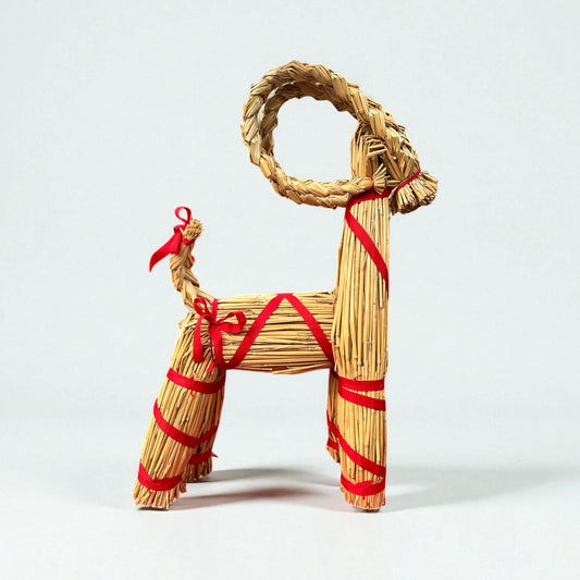 Woven straw goat figure with red ribbons on a white background