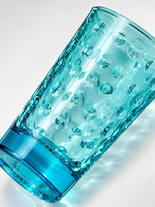 Close-up of a vintage ice blue highball glass tilted diagonally, showing its circular optic pattern and thick glass base.