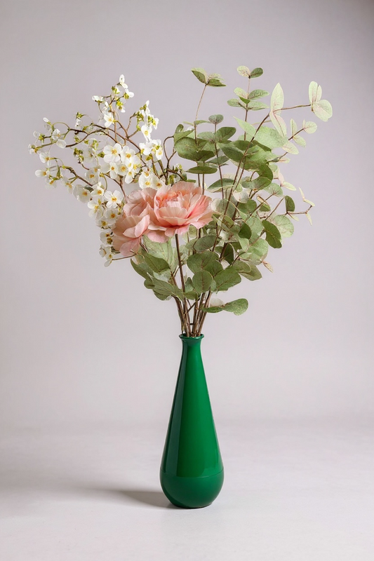 Green vase with pink flower and greenery on a light gray background