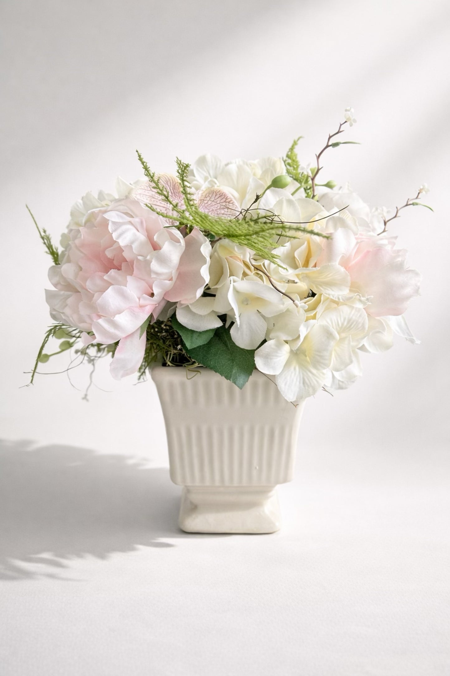 Elegant faux flower arrangement in a white ceramic vase, featuring peonies, hydrangeas, and greenery.