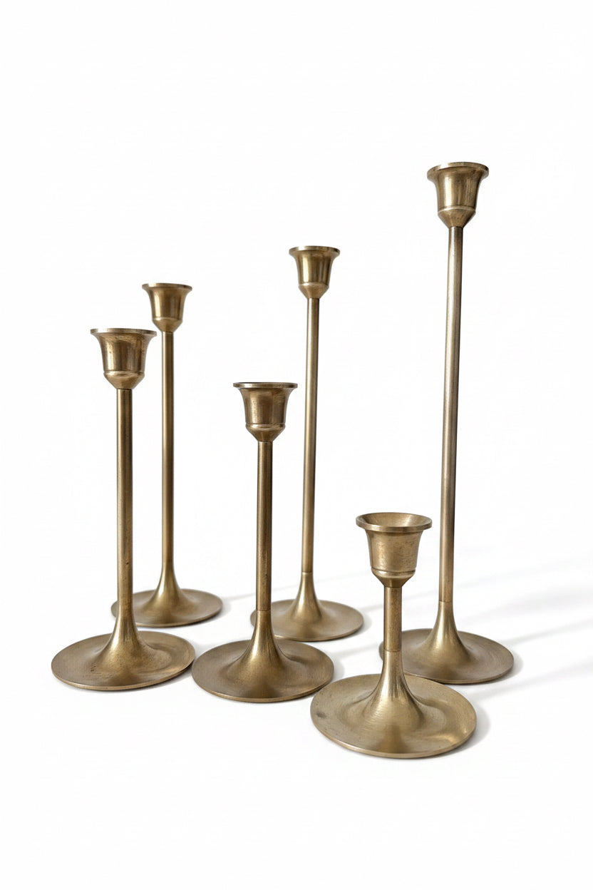 Gold candlesticks on a table with decorative items and flowers in the background