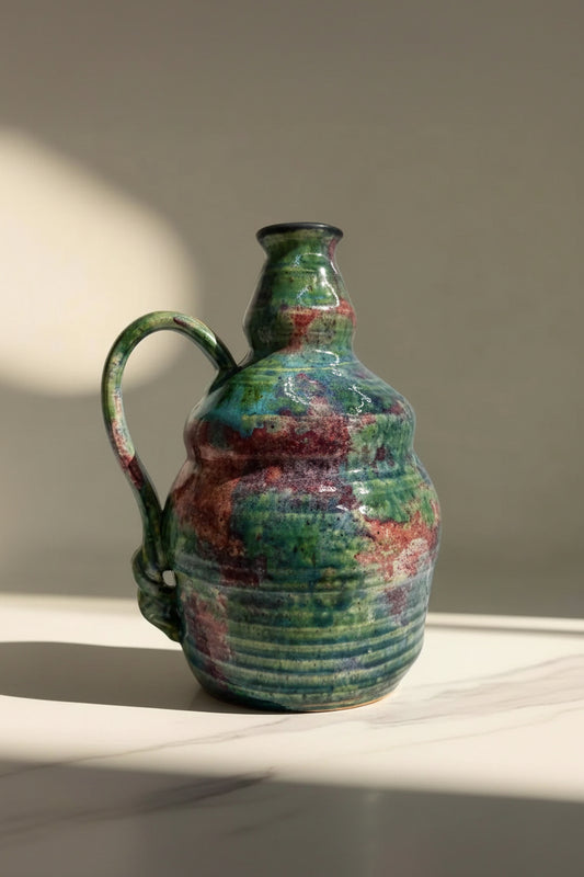 Colorful ceramic vase in green and red, with a unique textured design and curved handle.