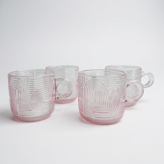 Set of four pink glass mugs with geometric patterns on a white background