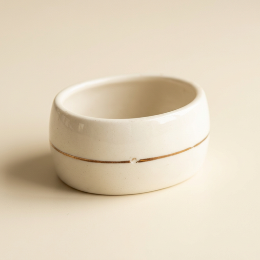 Close-up of an ivory napkin ring showing its rounded profile and a small worn gap in the gold-tone center stripe.