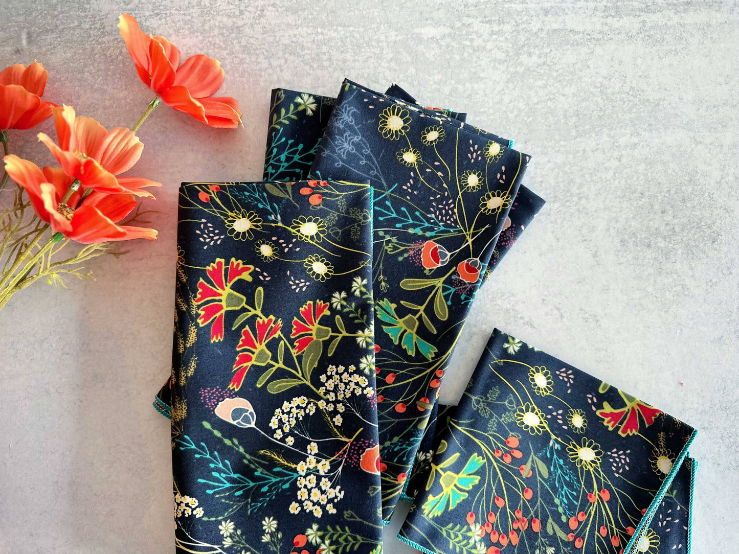 Set of floral cotton napkins in dark blue with colorful flower patterns, perfect for dining decor.