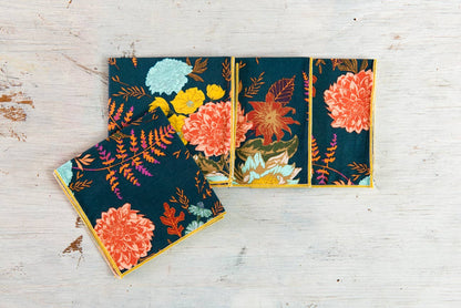 Set of floral fabric napkins in dark teal with vibrant orange and yellow flowers, perfect for dining decor.