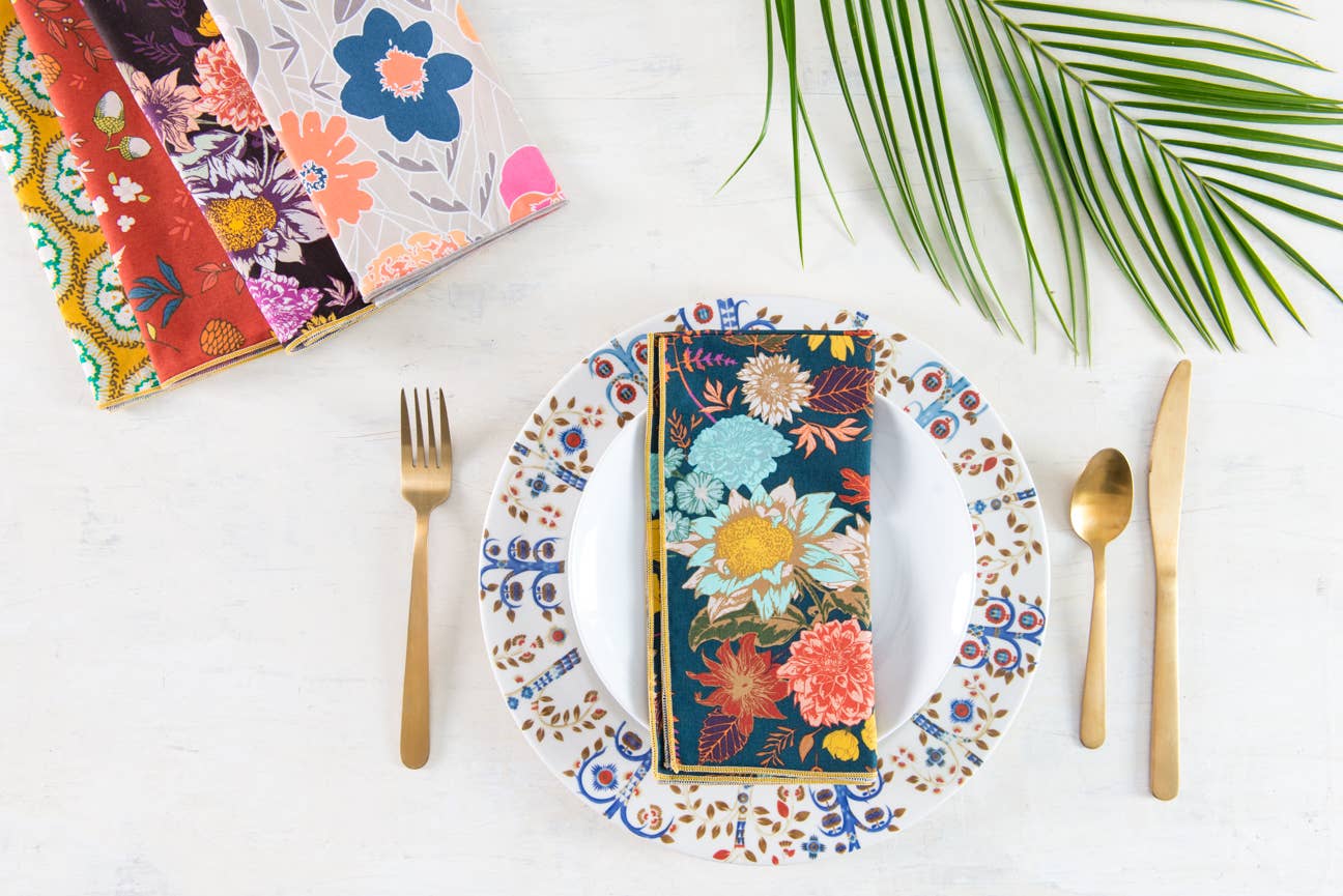 Floral fabric napkin in vibrant colors, placed on a decorative plate with gold cutlery.