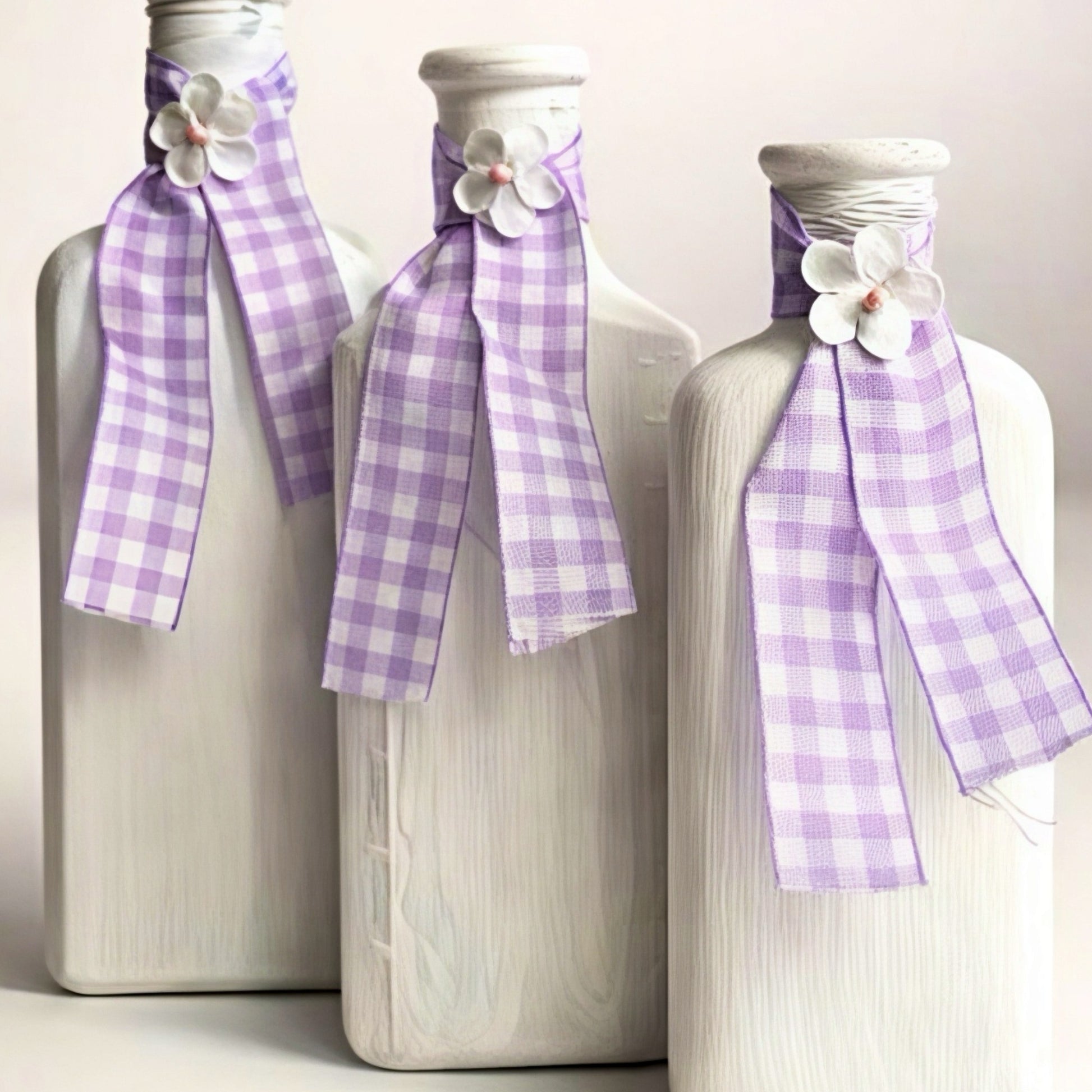 Set of three decorative white glass bottles with purple checkered ribbons and floral accents.