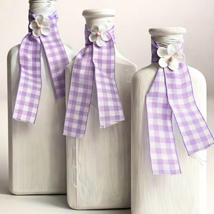 Set of three decorative white glass bottles with purple checkered ribbons and floral accents.