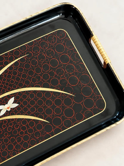 Close-up of the tray’s cane-wrapped handle, worn gold-tone rim, and red overlapping-circle pattern on glossy black.

