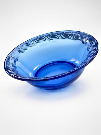Vintage cobalt blue glass pie dish with a wide rim and raised scrolling leaf pattern, shown at an angle.

