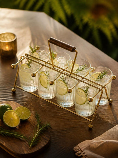 Set of six glasses with lemon slices and herbs in a gold caddy on a wooden table. Gold vintage mid century modern atomic age drink carrier with a wooden handle on a white background