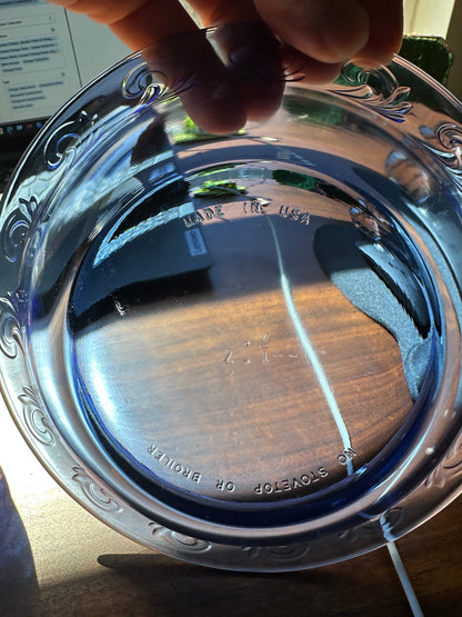 Cobalt blue glass dish held toward the light to show its underside, raised rim pattern, and molded manufacturing marks.
