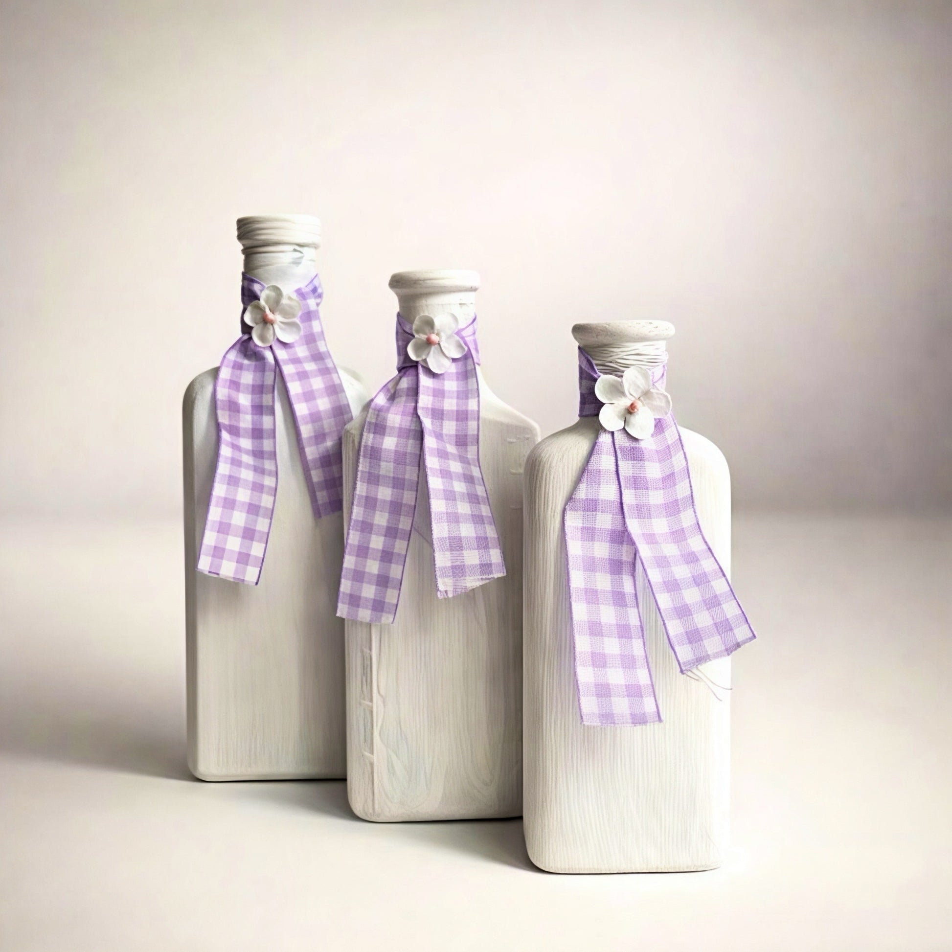 Set of three decorative white glass bottles with lavender checkered ribbons and floral accents.