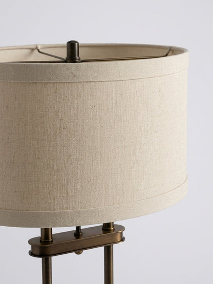 Detailed shot of an oatmeal linen oval lamp shade displaying natural fabric weave, top finial, and upper antique brass column hardware.