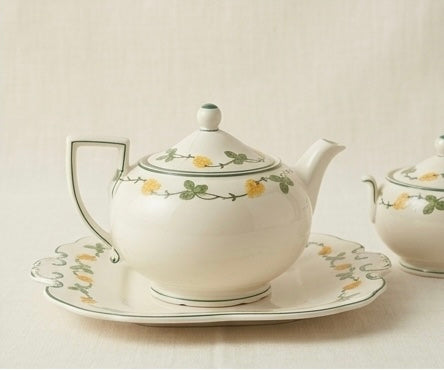 White teapot with floral design on a matching saucer and small bowl on a light background