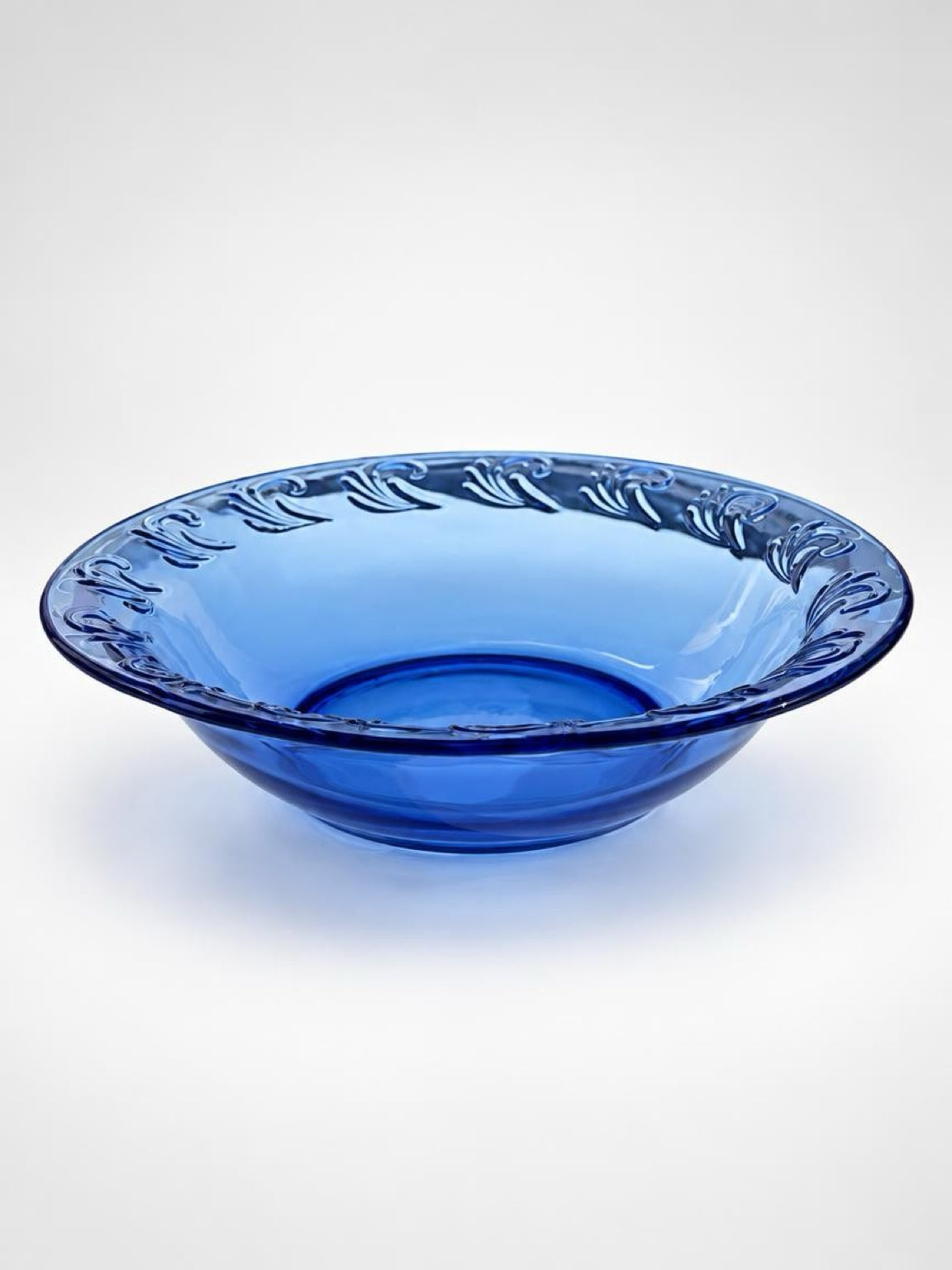 Side view of a vintage cobalt blue glass pie dish showing its shallow profile, sloping sides, and wide patterned rim.
