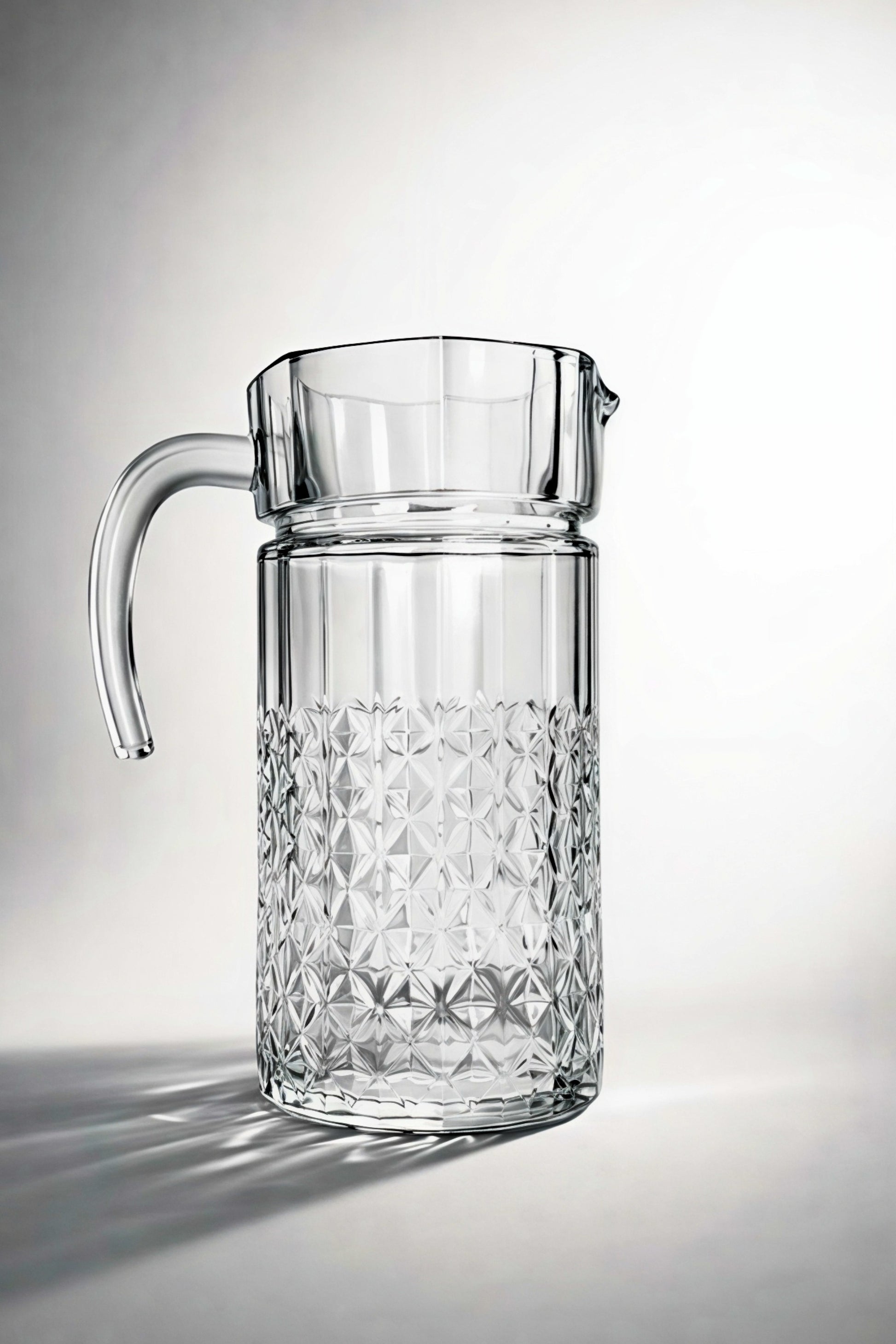 Clear glass pitcher with diamond pattern on a light gray background