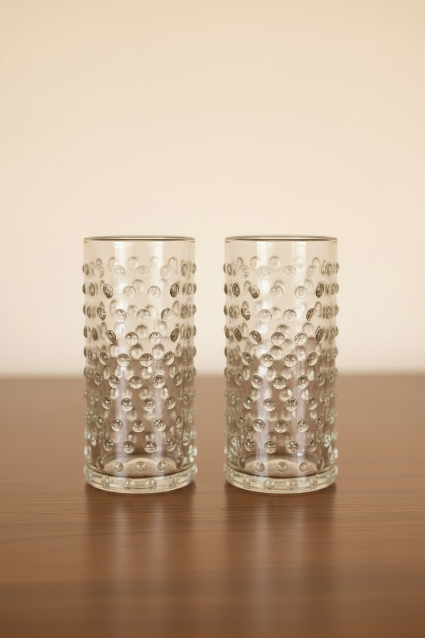 Set of 2 clear cylinder highball glasses with raised hobnail beaded texture sitting on a dark wooden tabletop, 6 inches tall.