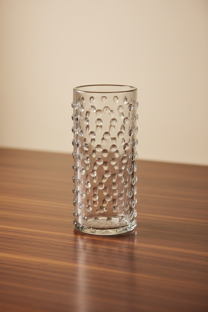 Set of 2 clear cylinder highball glasses with raised hobnail beaded texture sitting on a dark wooden tabletop, 6 inches tall. Arranged on wooden surface 