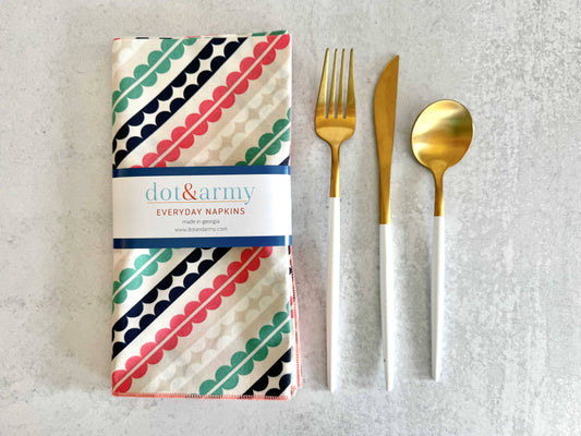 Pack of dot&amy napkins with gold fork and spoon on a textured surface