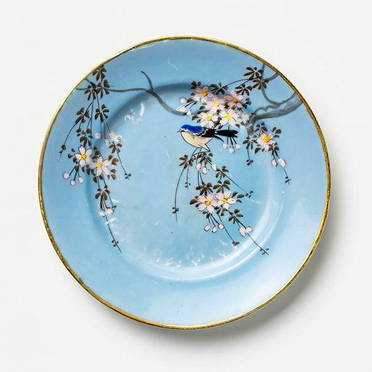 A 6-inch vintage Japanese porcelain plate featuring a hand-painted blue songbird on a cherry blossom branch against a vibrant sky-blue background with a gold rim.