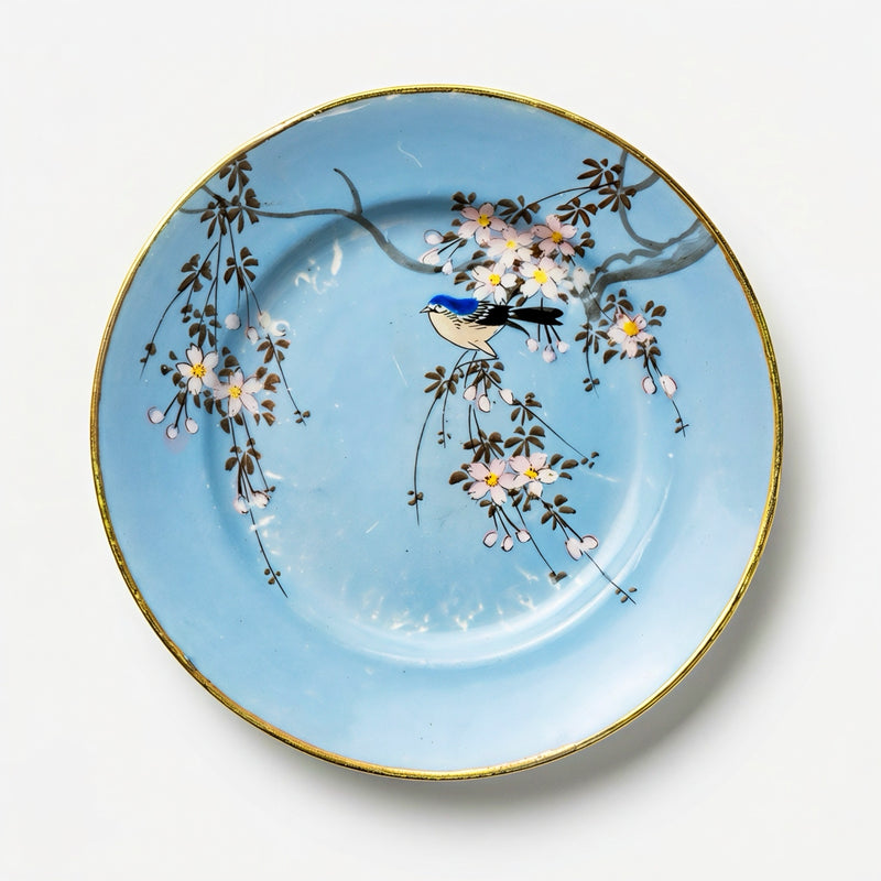 A 6-inch vintage Japanese porcelain plate featuring a hand-painted blue songbird on a cherry blossom branch against a vibrant sky-blue background with a gold rim.