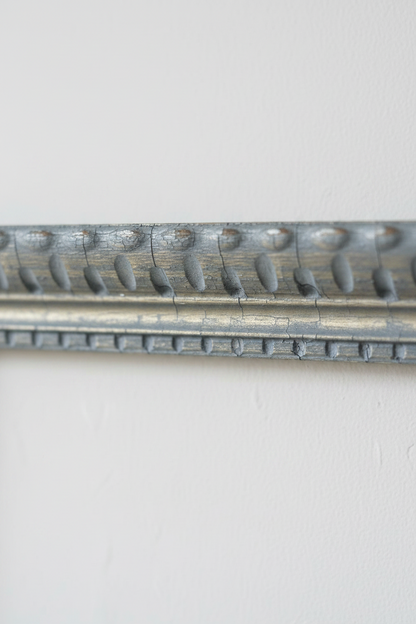 Corner detail of second vintage carved wood frame showing acanthus scroll relief molding in silver grey wash with warm gold undertones on a wood surface