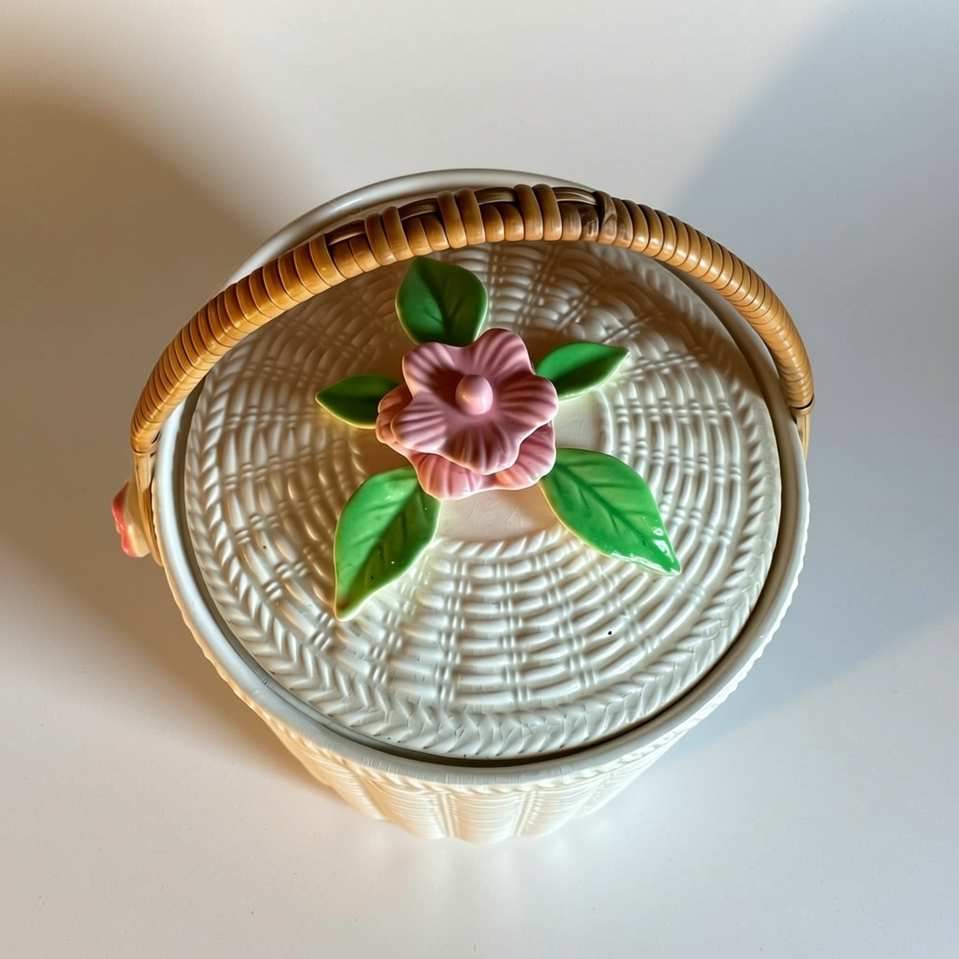Vintage white basket with pink flower lid and woven handle, ideal for decorative storage.