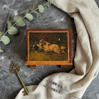 Vintage mid-century cedar keepsake box with inset hunting dog lithograph lid and gilt San Diego Cal script, three-quarter view showing exposed finger-joint corners and carved fluted block feet
