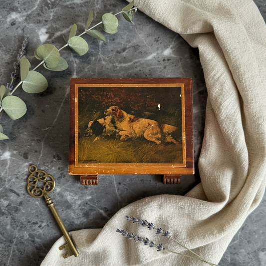 Vintage mid-century cedar keepsake box with inset hunting dog lithograph lid and gilt San Diego Cal script, three-quarter view showing exposed finger-joint corners and carved fluted block feet