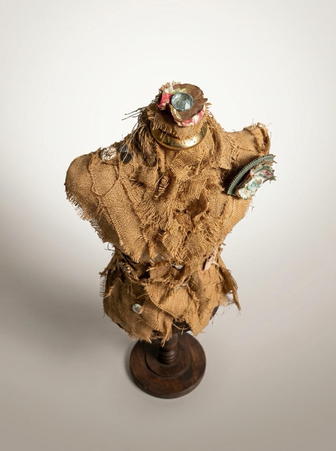  Overhead view of burlap dress form sculpture showing decorative neck ornament, brass-toned collar, and floral rosette.