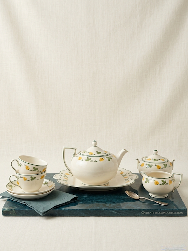 Tea set with teapot, cups, and saucers on a dark surface against a beige background