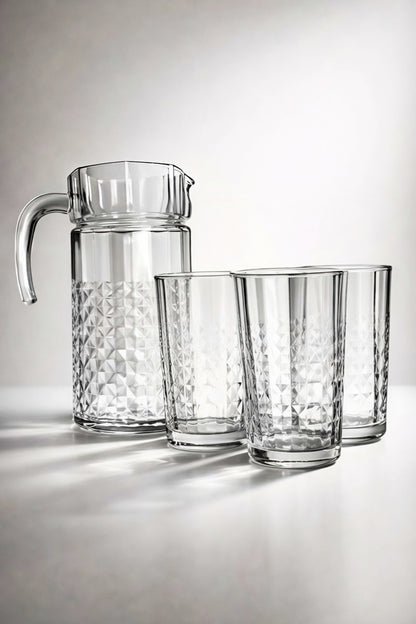 Clear glass pitcher and three glasses on a light gray background