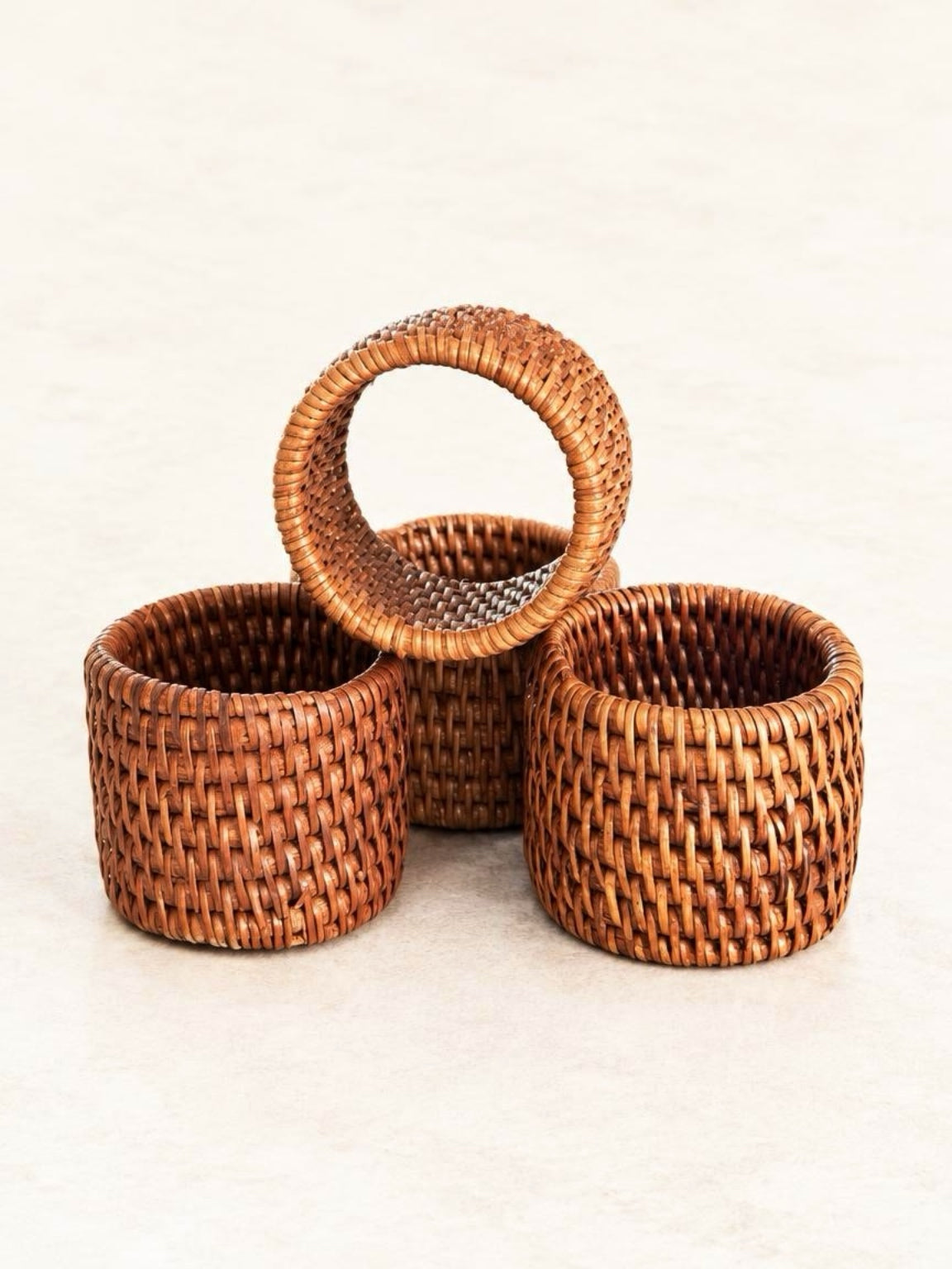 Set of four honey-brown handwoven rattan napkin rings with wide basketweave bands and neatly wrapped edges.
