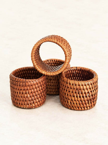 Set of four honey-brown handwoven rattan napkin rings with wide basketweave bands and neatly wrapped edges.
