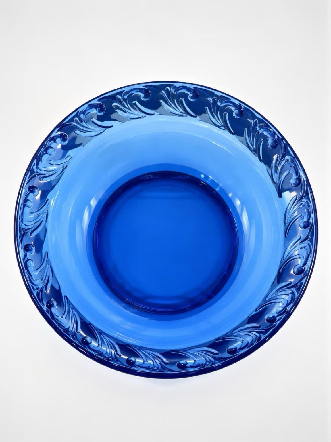 Overhead view of a cobalt blue glass pie dish showing its round center and raised scrolling leaf border.
