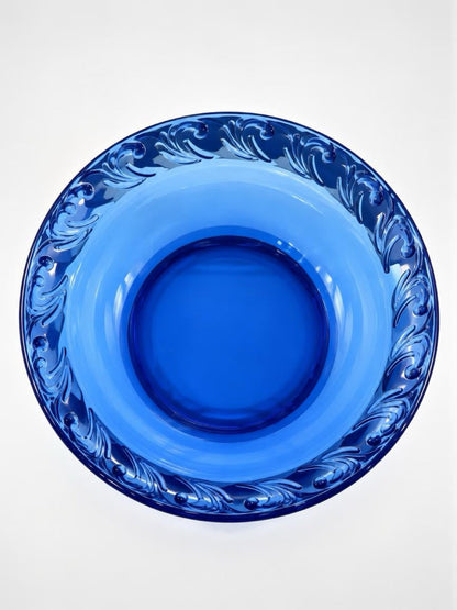 Overhead view of a cobalt blue glass pie dish showing its round center and raised scrolling leaf border.
