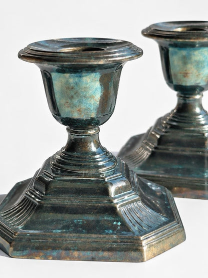 Close-up of a silverplate candlestick showing fluted corners, a stepped octagonal base, and blue-green tarnish.