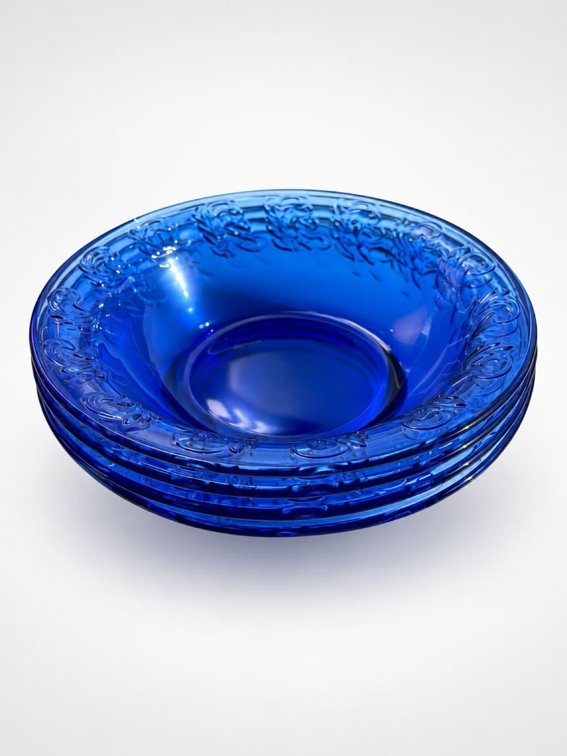 Set of four vintage cobalt blue glass pie dishes stacked together, showing their decorative raised rims.
