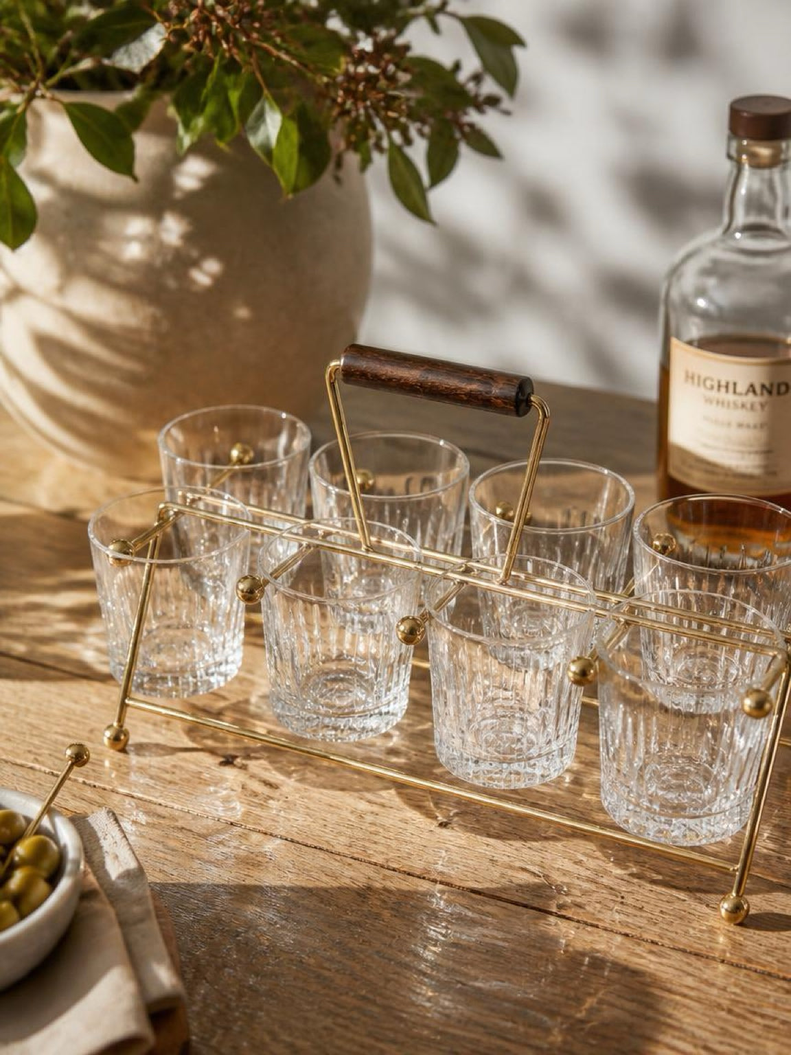 Set of clear glasses on a gold tray with a bottle of Highland Park whisky on a wooden table. Gold vintage mid century modern atomic age drink carrier with a wooden handle on a white background