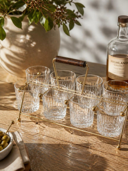 Set of clear glasses on a gold tray with a bottle of Highland Park whisky on a wooden table. Gold vintage mid century modern atomic age drink carrier with a wooden handle on a white background