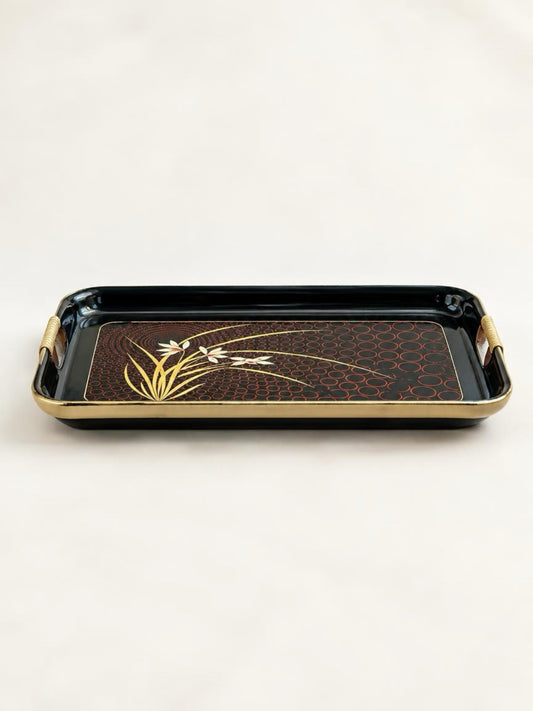 Low front view of a black lacquer floral serving tray showing raised sides, gold-tone rim, and cane-wrapped cut-out handles.
