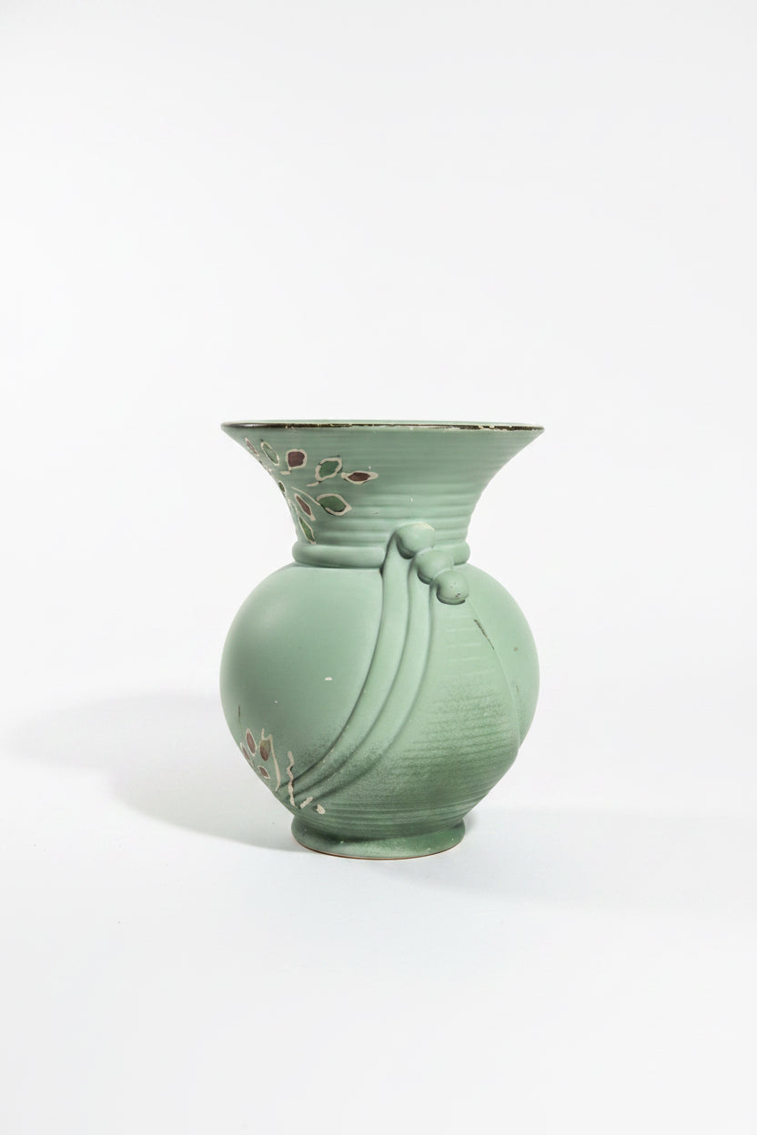 Alternate view of a vintage art pottery vase in matte sage green on a crisp white backdrop. This side highlights detailed hand-painted tube-lined illustrations of stylized crocus or tulip flowers in soft orange, yellow, and white at the base, with slender brown branches extending up to the flared rim.