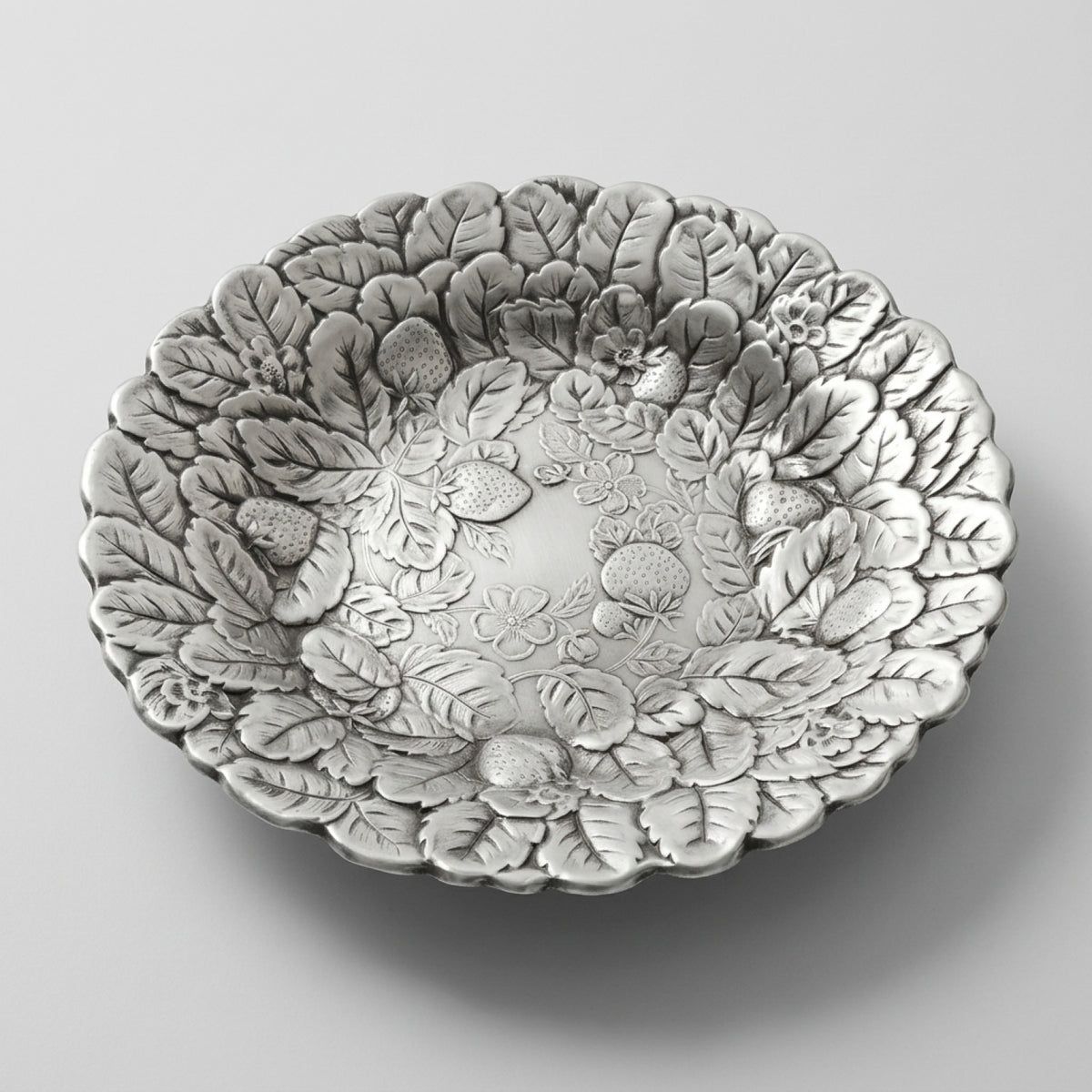 An angled profile edit of a mid century silverplate tray with an embossed berry motif serving bowl design.