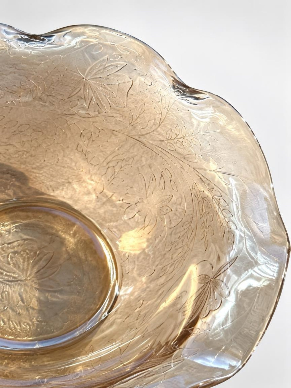Close-up of molded flowers and leafy vines on the amber glass bowl, with pearlescent reflections along the ruffled rim.